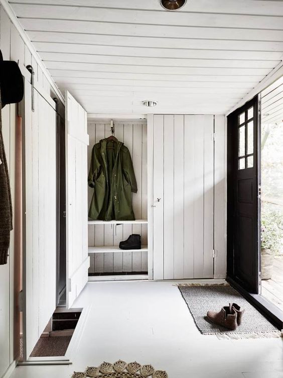 A cozy and simple entryway with whitewashed wood plank walls, ceiling and storage furniture