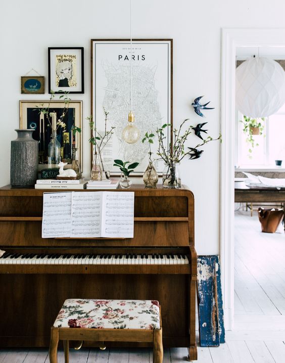 a cool piano, an upholstered stool and a gallery wall with signs and artworks, greenery and flowers in vases on display