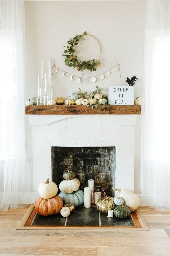 a modern and natural mantel with pumpkin, eucalyptus, candles, signs and a fake bird