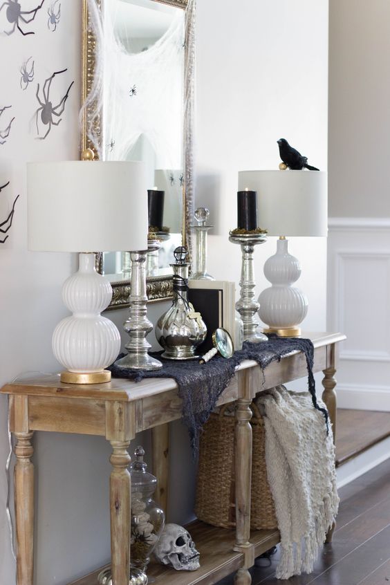 a rustic console with a bird, a skull, some spiderweb and black candles in tall candleholders