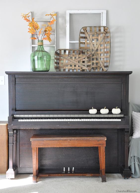 a fall display with frames, fake pumpkins, fallfoliage and wood strip bowls on the piano