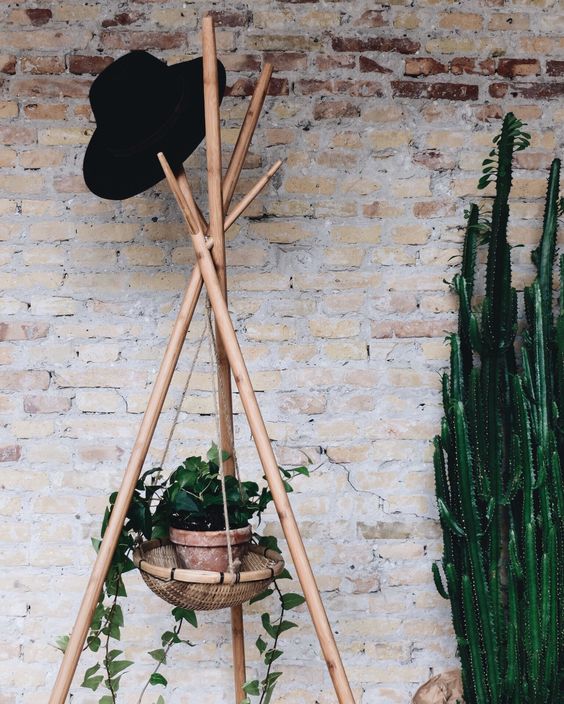 a wooden coat rack made of wood sticks and with a suspended planter in a basket to enliven your space