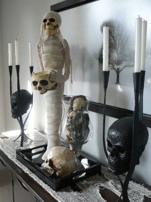 a spooky console display with skulls and a mummy plus candles and a haunted scenery on the artwork