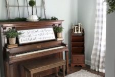 16 a rustic piano and a stool, an evergreen runner, potted greenery and an artwork placed on the piano