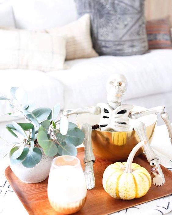 a modern fall display with eucalyptus, pumpkins, candles, a skeleton in a gold bowl on a tray