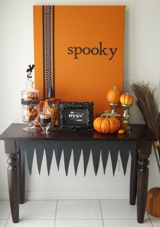 a stylish black and orange console with an artwork, faux pumpkins and glass jars with candies
