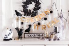 a stylish black, white and gold console with a bunting, a wreath, fake birds and a pumpkin with spiders