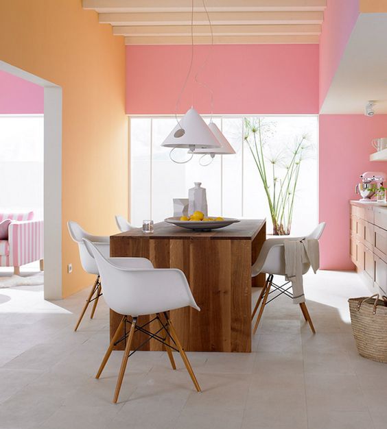 Color blocked kitchen walls in pastel pink and orange plus wooden furniture for an inviting eat in space