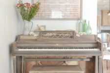 20 a vintage piano in taupe and a mtching stool, some bottles, a metal jug with blooms and some notepaper as an artwork