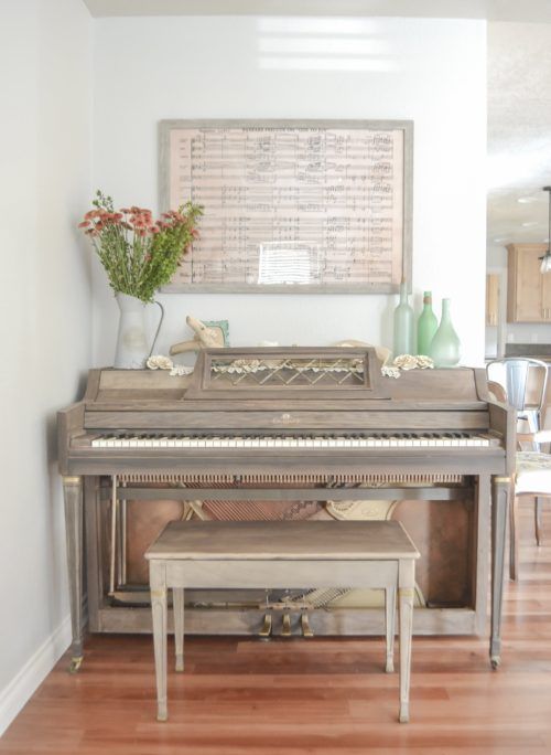 a vintage piano in taupe and a mtching stool, some bottles, a metal jug with blooms and some notepaper as an artwork
