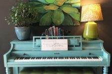 21 a bright blue piano, a potted plant, a lamp, a stack of books and a bold succulent artwork for a touch of color and interest
