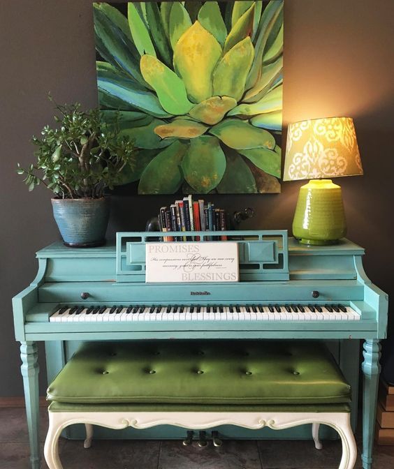 a bright blue piano, a potted plant, a lamp, a stack of books and a bold succulent artwork for a touch of color and interest