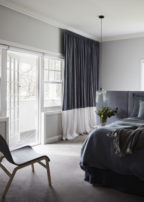 A monochromatic grey and white space with color blocking   a headboard wall and curtains