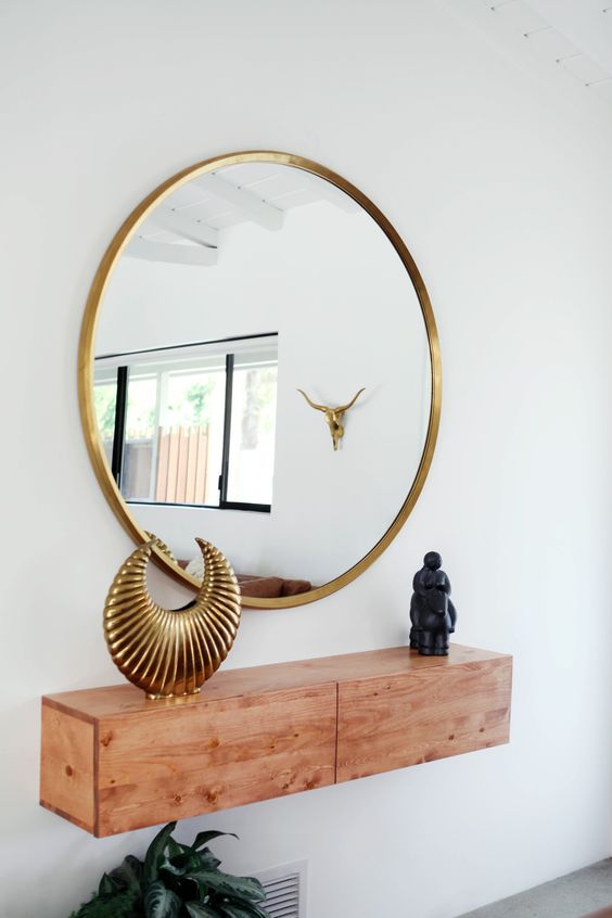 A stylish light colored wood floating console table and a brass framed mirror for a chic entryway