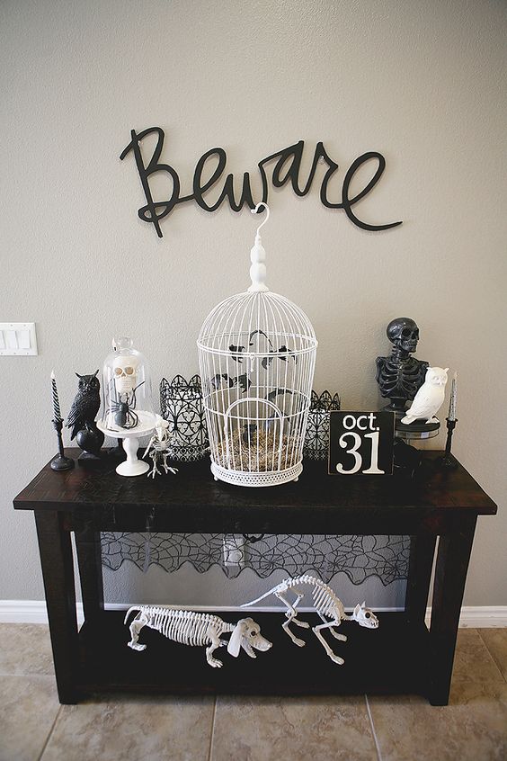 a vintage console table with black and white skeletons of various animals, a cage with bats and black calligraphy over the table