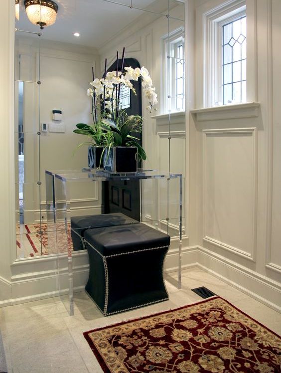 a mirrored wall with an acrylic console and a black ottoman looks very interesting and eye-catchy