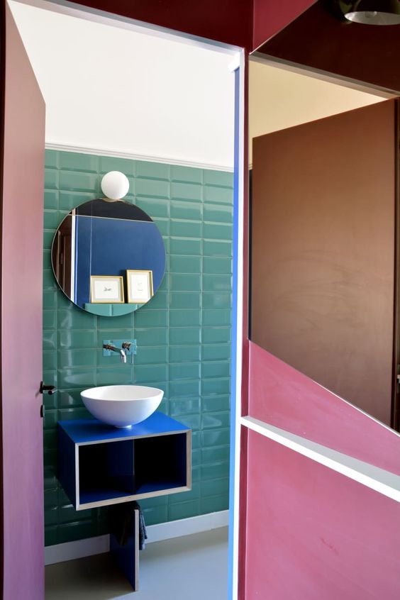 Green tiles and a bright blue vanity with an eye cathcy shape make the powder room extra bold