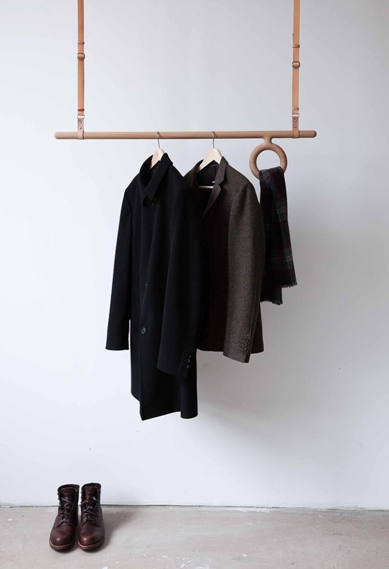 a modern leather and wood coat rack attached to the ceiling is an adjustable piece that offers space for accessories, too
