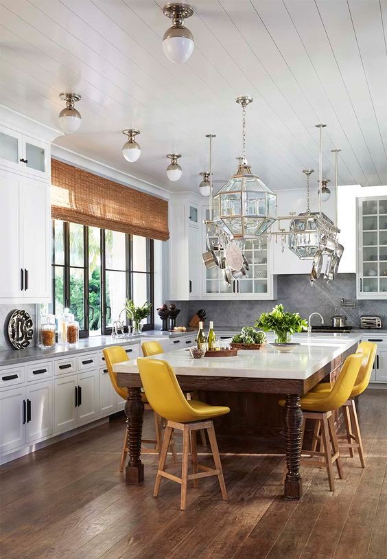 an oversized rustic kitchen island of stained wood and with a white tabletop is used as a dining table