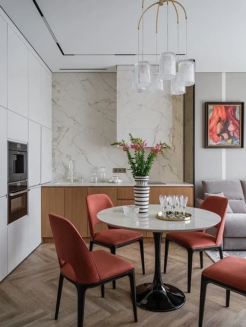 A bright eat in kitchen with stained cabinets, a white stone backsplash and hood, a round table and red chairs