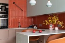 a colorful eat-in kitchen with taupe and mint cabinetry, a countertop for earing, pendant lamps and a bold red backsplash