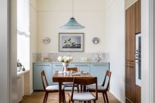 a lovely Scandi kitchen with pastel blue lower cabinets, a grey stone backsplash, a herringbone floor and a rich-stained dining set