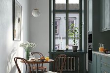 a small and pretty Scandi kitchen with dark green cabinets, a printed tile floor, vintage dining set and some chic decor