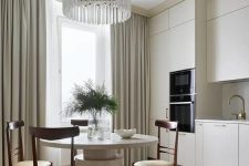 a sophisticated neutral eat-in kitchen with creamy cabinets, a round table, rich-stained chairs and a crystal chandelier