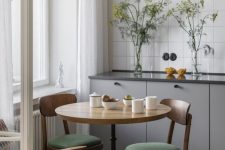 a tiny Scandi eat-in kitchen with lower grey cabinets, a white square tile backsplash, a vintage table and matching chairs plus a green tile floor