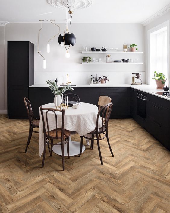 An elegant eat in kitchen with black lower cabinets, white walls and shelves, a herringbone floor and a vintage dining set