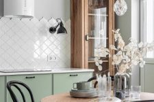 an ethereal kitchen with light green lower cabinets, an arabesque tile backsplash, a stained buffet and table and cool pendant lamps