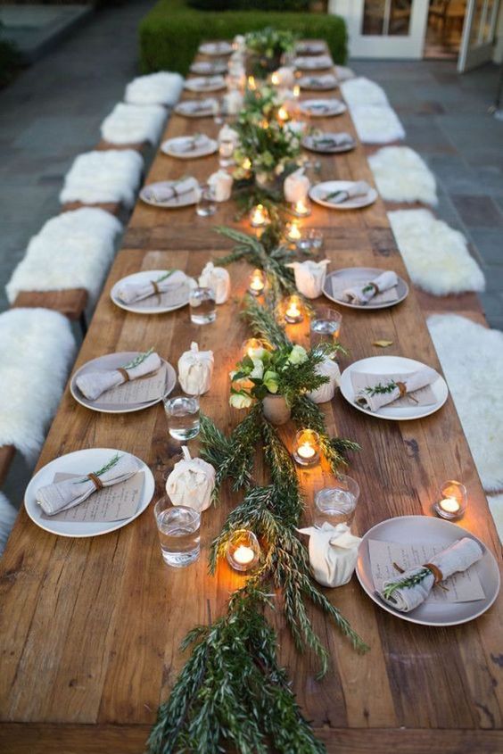 a natural tablescape with a greenery runner, candles in lanterns and napkins, some white blooms for a festive feel