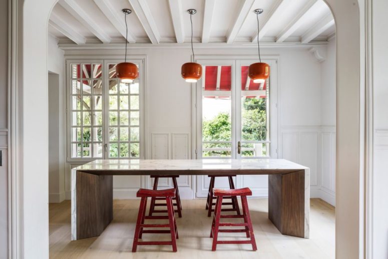 A small breakfast space is done with red stools. orange pendant lamps and a table of wood and marble
