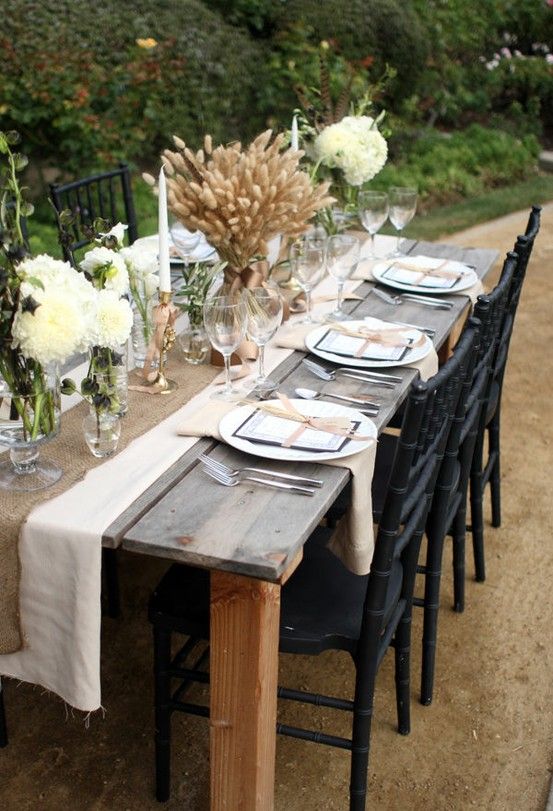 a burlap table runner, white blooms with feathers and a large wheat centerpiece with ribbon for a rustic fee