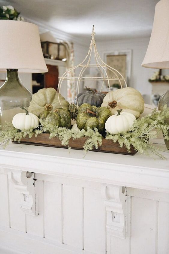 a farmhouse styled Thanksgiving decoration of a wooden crate, greenery, white and green pumpkins and a fake cage