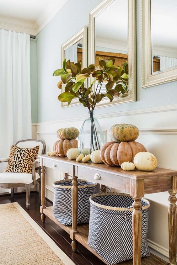 a natural console with fabric baskets, real pumpkins and branches with leaves in a clear vase
