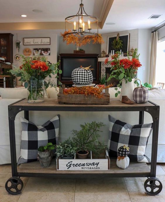 an industrial console with floral arrangements, fabric pumpkins, potted greenery and plaid pillows