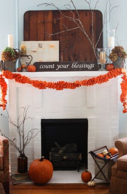 a large pallet, some orange pumpkins, an orange fabric garland and dried hydrangeas and firewood in the fireplace