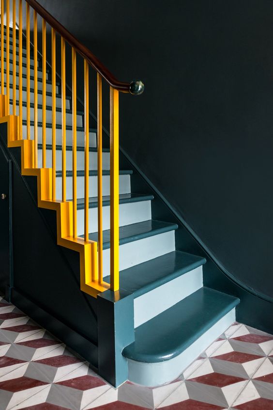 a staircase done in two shades of blue and spruced up with bold yellow railing for a contrast