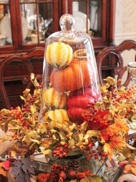 a rustic cloche display with fake pumpkins and peppers surrounded with foliage and berries for a vintage feel