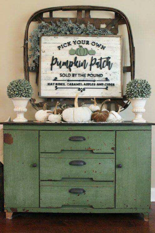 a vintage and rusty console with fabric pumpkins, faux greenery in pots and cool decor on the wall with a sign
