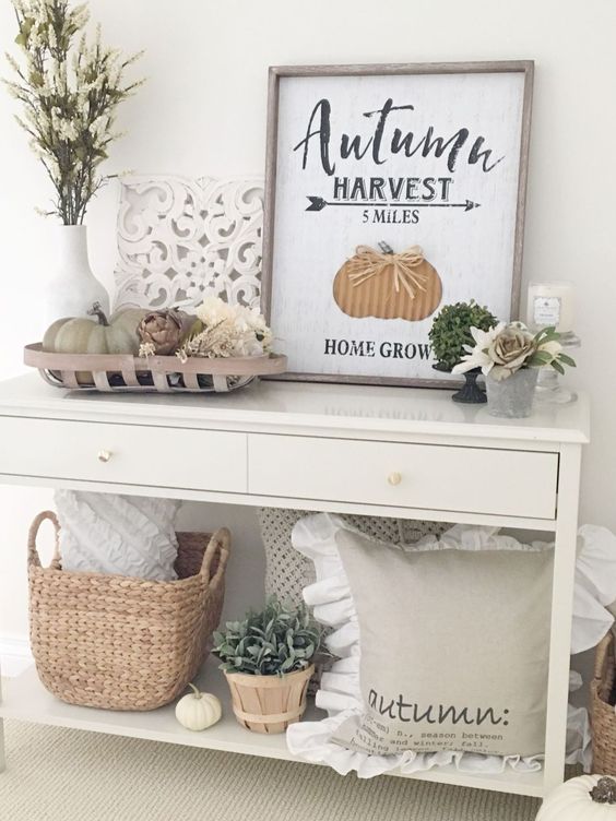 a simple console with faux pumpkins, a basket, a pillow, greenery and a fall sign plus fresh blooms