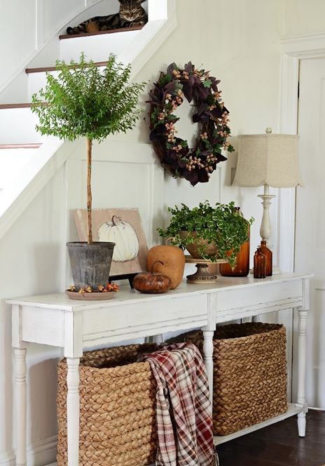 a vintage console with baskets, faux pumpkins, potted plants and a wreath of fake leaves and berries