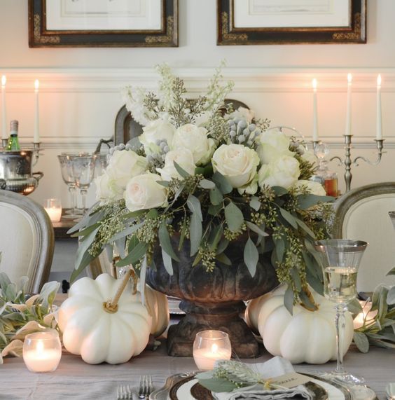 a luxurious Thanksgiving centerpiece with a vintage urn, seeded eucalyptus, white roses, berries and white pumpkins around