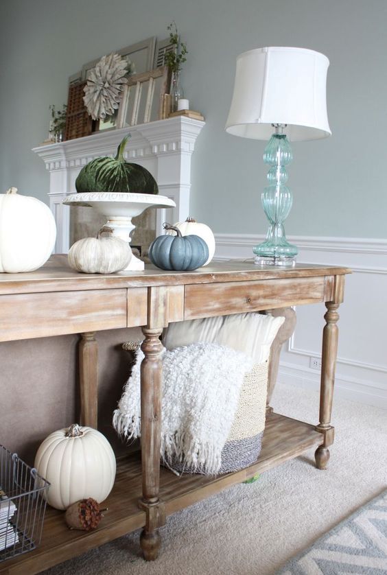 a vintage console with faux pumpkins including fabric ones and a basket with pillows and blankets