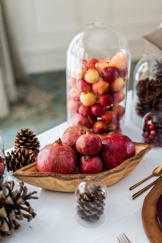 a cloche filled with little fall apples and a centerpiece of a wooden bowl with pomegranates plus pinecones