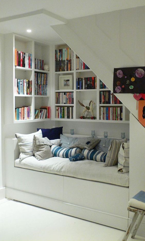 an under the stairs nook for reading, with bookshelves and a large upholstered bench to enjoy