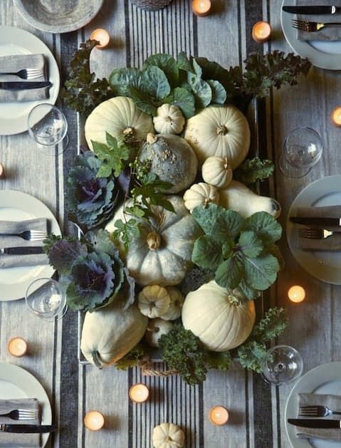 a rustic harvest Thanksgiving centerpiece with white and green pumpkins, various kinds of cabbage and candles around