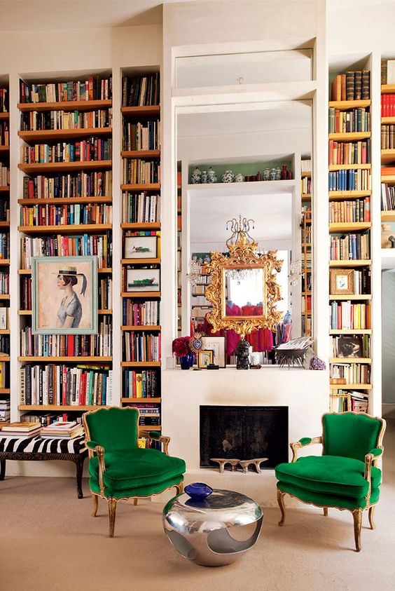 a maximalist space with lots of books by the fireplace and colorful furniture and metallics