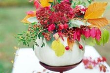 21 a Thanksgiving centerpiece made of a wooden stand, a white pumpkin, orange leaves and hot red berries plus leaves